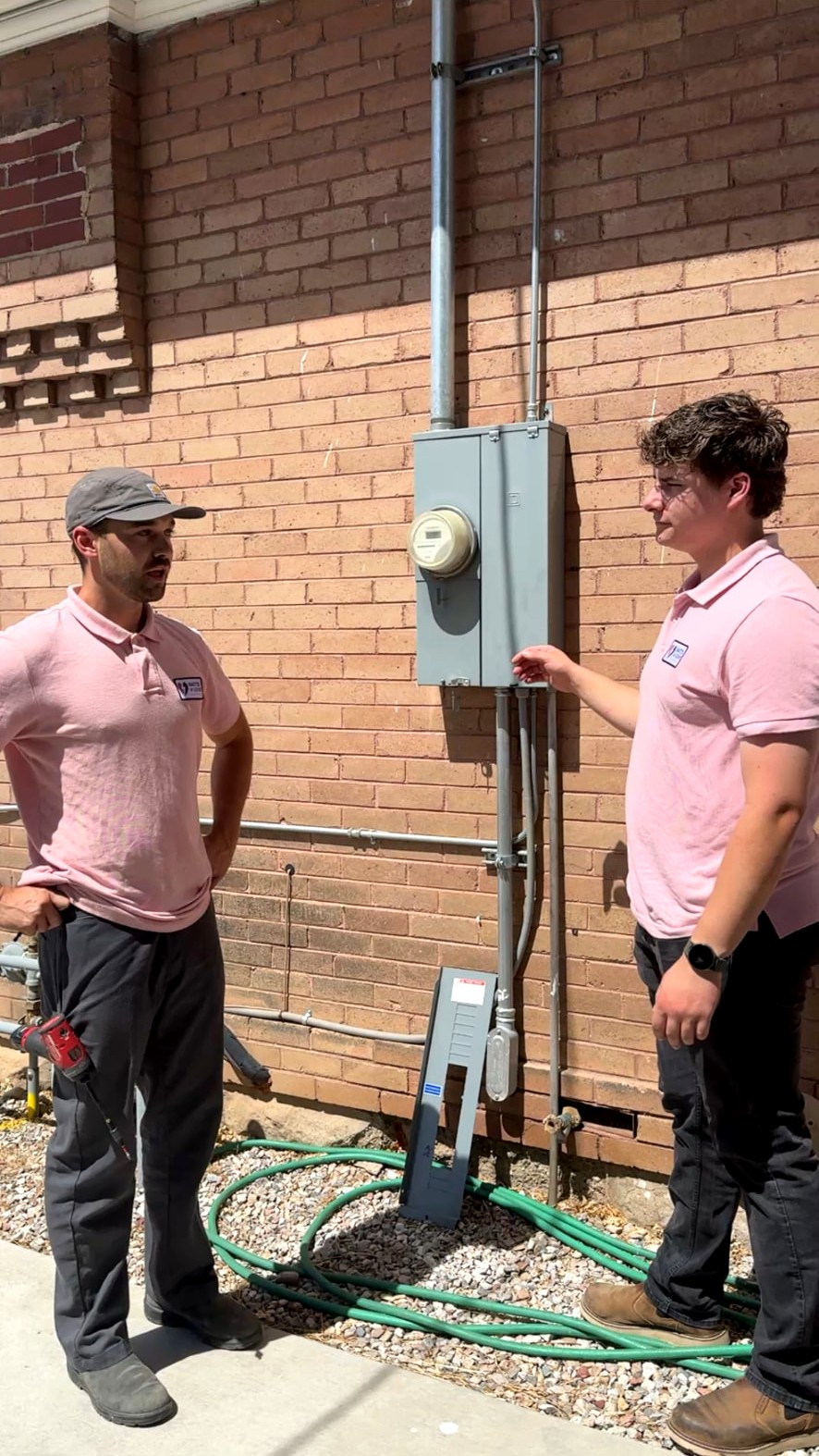 Watts of Love Electric technicians standing beside residential electrical meter equipment on a brick home.